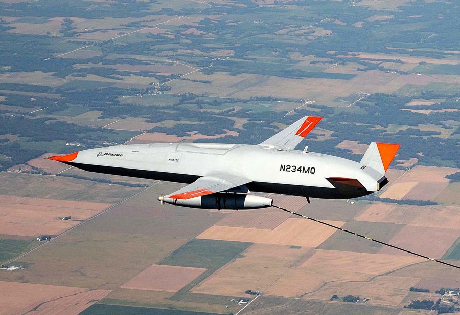A white MQ-25 drone flying over farmland