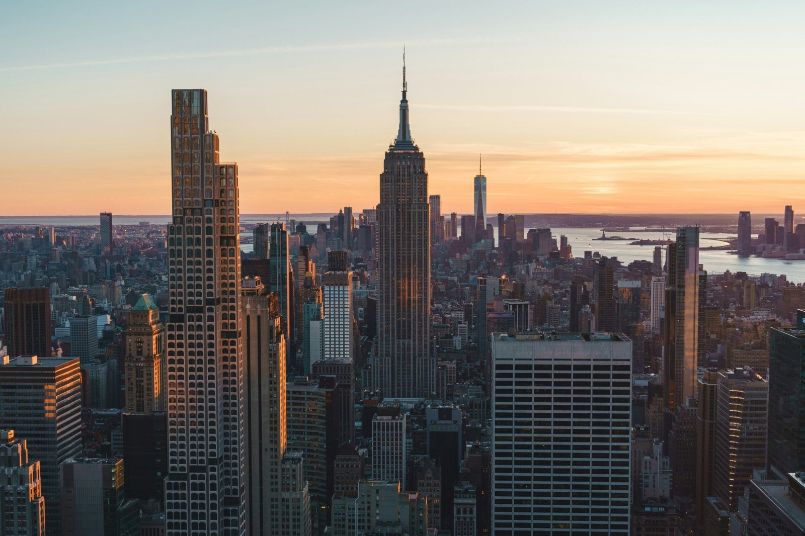 The Manhattan skyline at sunset, with the Empire State Building at the center and the harbor beyond
