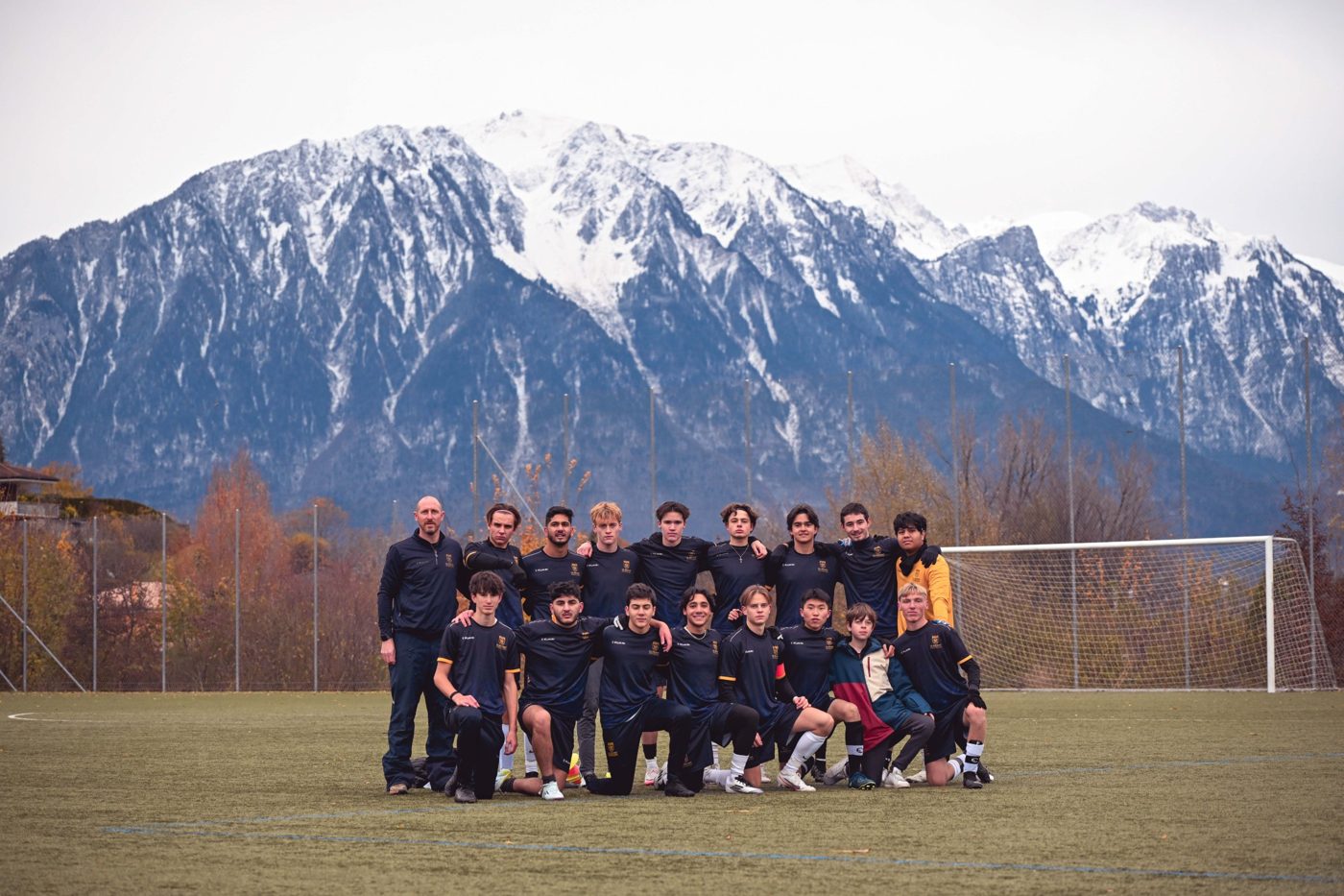 A school soccer team posing on a pitch below snow-covered Swiss mountains