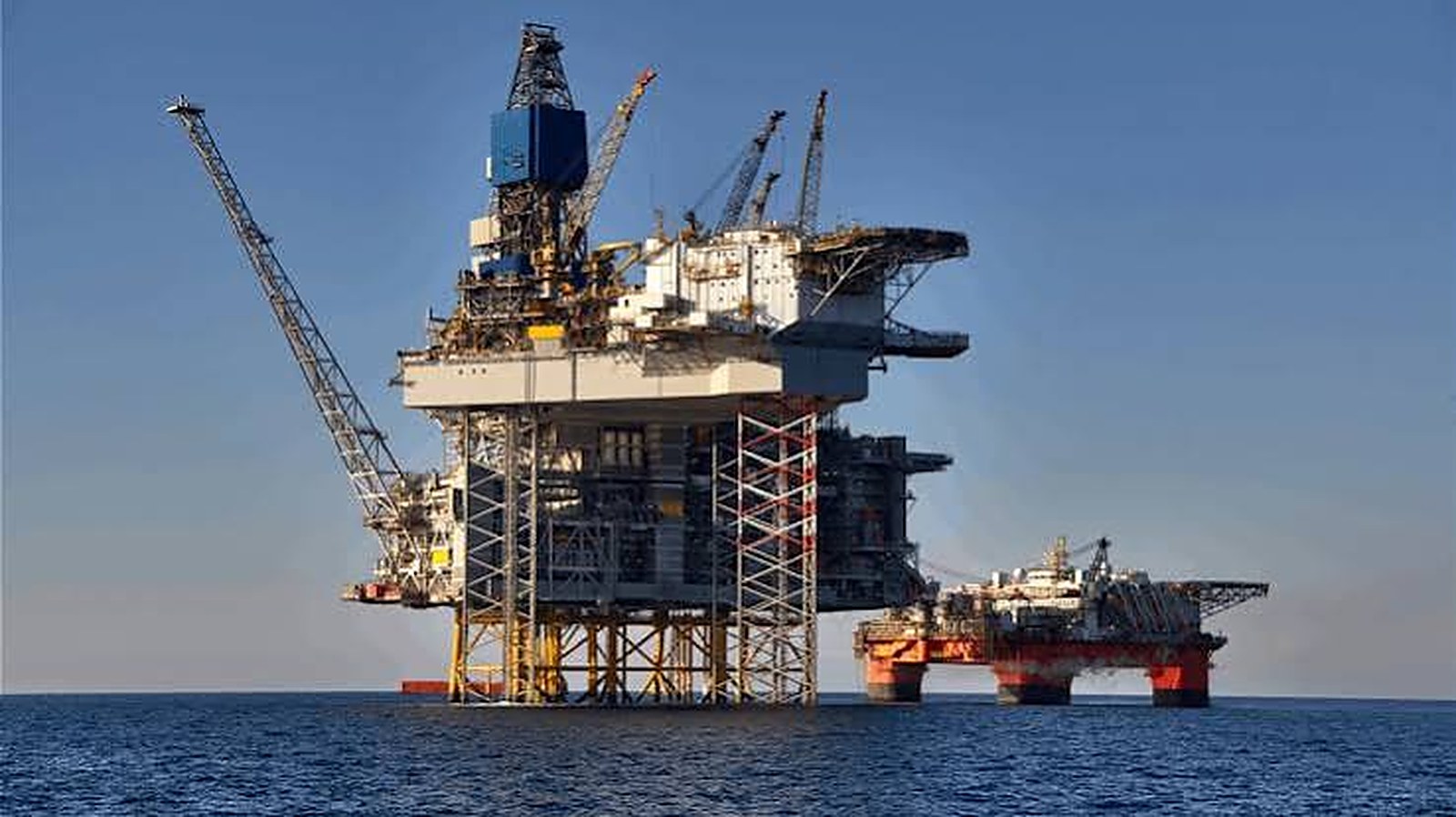 An offshore oil and gas platform standing in calm blue water with a support vessel beside it